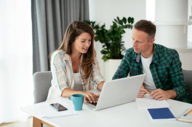 Erkek ve kadın evde dizüstü bilgisayar kullanarak çalışıyor.