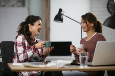 Açık uzay ofisinde konuşan ve gülen mutlu iş kadınları