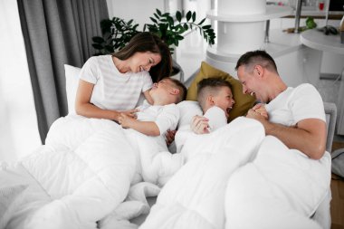 Genç bir aile yatakta eğleniyor. Oğulları yatakta dinlenen mutlu ebeveynler..