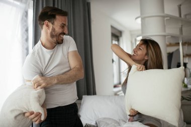 Genç çift yatakta yastık kavgası yapıyor. Mutlu çift evde eğleniyor.