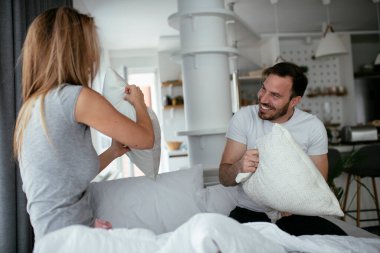 Genç çift yatakta yastık kavgası yapıyor. Mutlu çift evde eğleniyor.