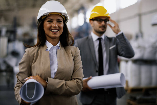 Businessman and businesswoman in factory. Two professional people with helmets working in quality control in factory production line.