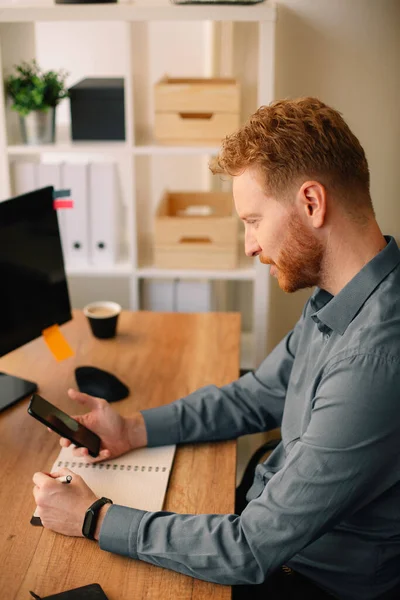 handsome businessman with ginger hair using smartphone in the office