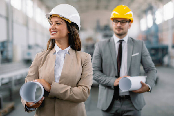 Businessman and businesswoman in factory. Two professional people with helmets working in quality control in factory production line.