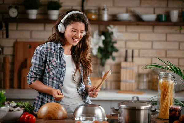 Sevimli, sevimli, neşeli, güzel, modaya uygun, modaya uygun, mutfakta müzik dinleyen kız. Mutfakta şarkı söyleyen genç mutlu kadın.