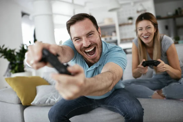 Husband and wife playing video game with joysticks in living room. Loving couple are playing video games at home.