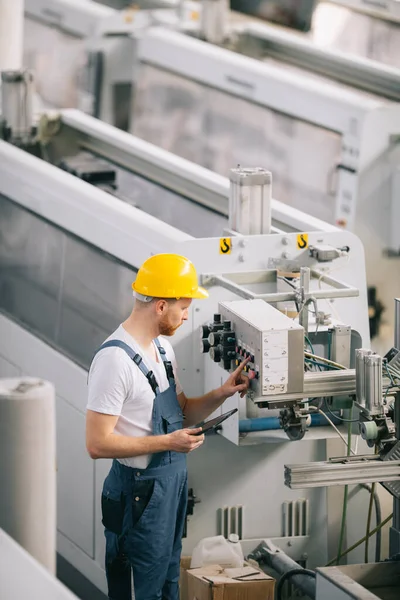 Üretim hattındaki fabrika işçisi. Fabrikada çalışan sarı kasklı adam..