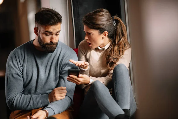 Angry couple or marriage fighting for a mobile phone at home. Jealous woman holding smartphone and showing message to his husband