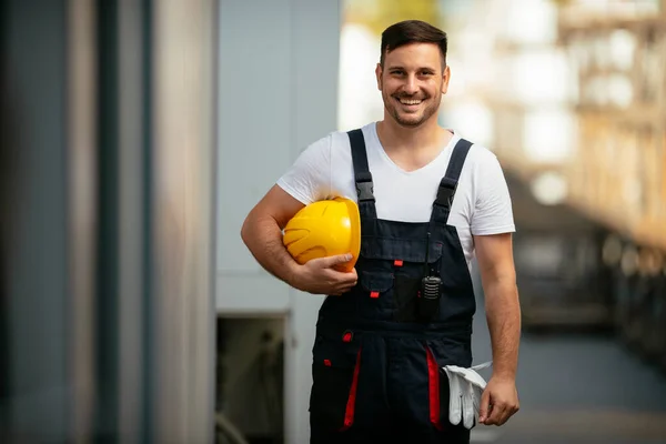 Portrait of smiling worker holding yellow helmet in hand