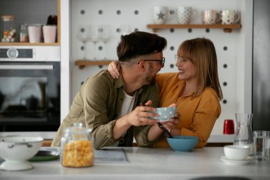 Genç çift evde kahvaltı hazırlıyor. Sevgi dolu çift mutfakta mısır gevreği yiyor..