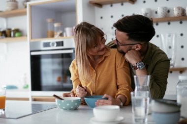 Genç çift evde kahvaltı hazırlıyor. Sevgi dolu çift mutfakta mısır gevreği yiyor..