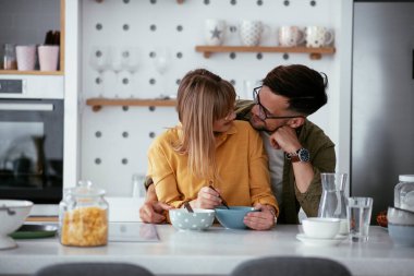 Genç çift evde kahvaltı hazırlıyor. Sevgi dolu çift mutfakta mısır gevreği yiyor..