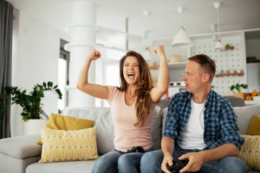 Erkek arkadaşı ve kız arkadaşı oturma odasında joysticklerle oyun oynuyorlar. Sevgili çift evde video oyunu oynuyor..