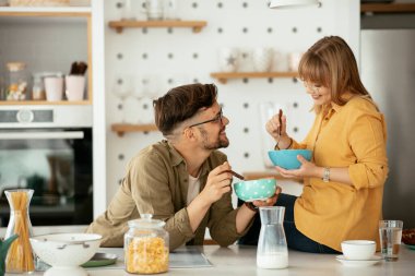 Genç çift evde kahvaltı hazırlıyor. Sevgi dolu çift mutfakta mısır gevreği yiyor..