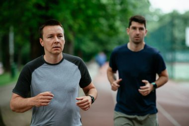 Gençler yarış pistinde antrenman yapıyor. İki genç arkadaş atletizm pistinde koşuyor.