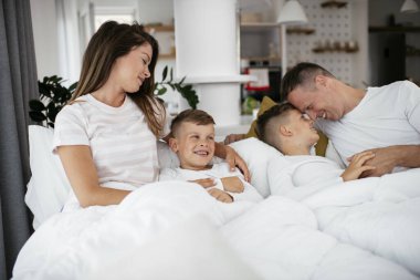 Genç bir aile yatakta eğleniyor. Oğulları yatakta dinlenen mutlu ebeveynler..