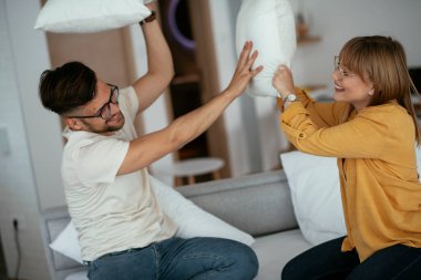 Erkek arkadaş ve kız arkadaş yatakta yastık kavgası yapıyor. Mutlu çift evde eğleniyor.