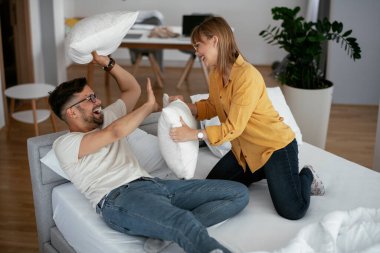 Erkek arkadaş ve kız arkadaş yatakta yastık kavgası yapıyor. Mutlu çift evde eğleniyor.