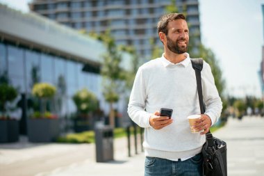 Yakışıklı genç işadamı telefon kullanıyor ve sokakta kahve içiyor.