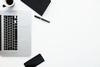 Ofis masasının en üst görüntüsü. Laptop, kahve ve malzeme dolu beyaz ofis masası..