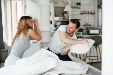 Genç çift yatakta yastık kavgası yapıyor. Mutlu çift evde eğleniyor.
