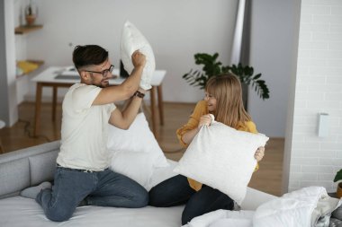 Erkek arkadaş ve kız arkadaş yatakta yastık kavgası yapıyor. Mutlu çift evde eğleniyor.