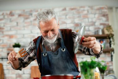 Yaşlı adam yemek yapıyor. Mutfakta kıdemli adam var..