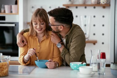 Genç çift evde kahvaltı hazırlıyor. Sevgi dolu çift mutfakta mısır gevreği yiyor..