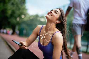 Egzersiz yapmaktan dinlenen güzel bir kadın. Genç sporcu kadın bankta oturuyor ve telefonu kullanıyor..