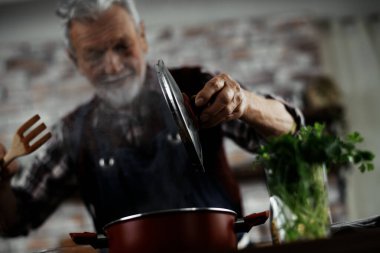 Yaşlı adam yemek yapıyor. Mutfakta kıdemli adam var..