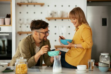 Genç çift evde kahvaltı hazırlıyor. Sevgi dolu çift mutfakta mısır gevreği yiyor..