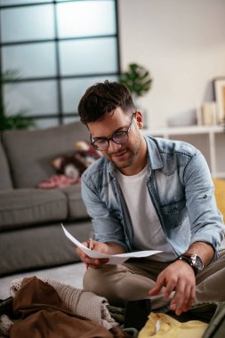 Giysilerini seyahat çantasına koyan gülümseyen genç adam. Yolculuğa hazırlanan adam.