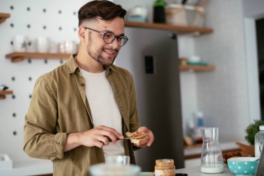 Genç adam kahvaltı yapıyor ve internette haberleri okuyor. Yakışıklı adam evde eğleniyor..