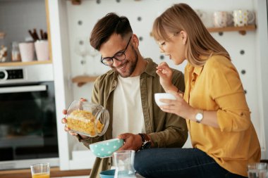 Genç çift evde kahvaltı hazırlıyor. Sevgi dolu çift mutfakta mısır gevreği yiyor..