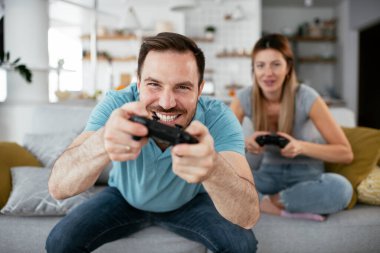 Karı koca oturma odasında joysticklerle oyun oynuyorlar. Sevgili çift evde video oyunu oynuyor..