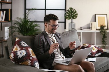 Evde pantolonsuz çalışan bir iş adamı. Genç adam video görüşmesi sırasında bilgisayarı kullanıyor..