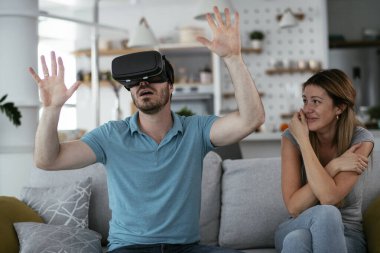 Mutlu çift oturma odasında sanal gerçeklik gözlükleriyle eğleniyor. Evde video oyunu oynayan ve eğlenen genç bir çift..