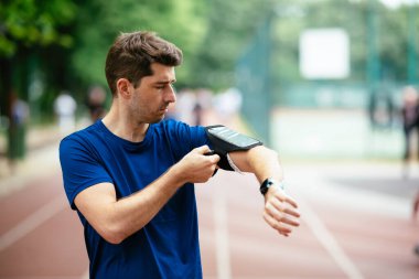 Genç adam antrenman sırasında kalp atışlarını kontrol ediyor. Genç adam atletizm pistinde egzersiz yapıyor..