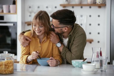 Genç çift evde kahvaltı hazırlıyor. Sevgi dolu çift mutfakta mısır gevreği yiyor..