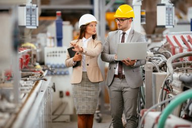 Fabrikadaki iş adamı ve iş kadını. Fabrika üretim hattında kalite kontrolde çalışan iki profesyonel insan..