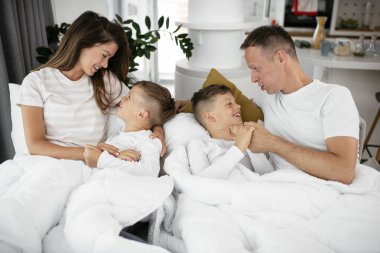 Genç bir aile yatakta eğleniyor. Oğulları yatakta dinlenen mutlu ebeveynler..