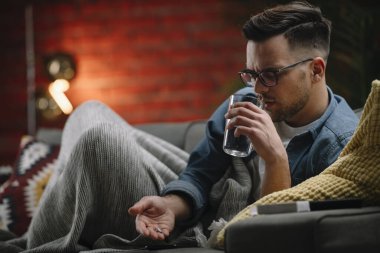 Genç adam evde hasta. Erkek, kanepede yatıyor ve ateşi var..