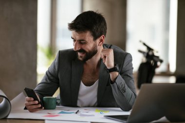İş adamı proje üzerinde çalışıyor. Ofiste akıllı telefon kullanan genç bir işadamı..