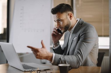 İş adamı telefonda iş konuşuyor. Genç işadamı ofiste telefonda konuşuyor..
