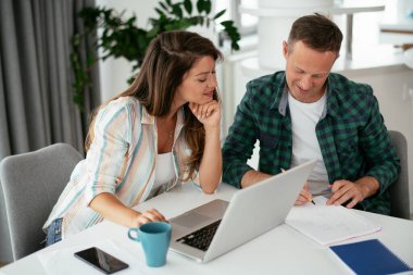 Erkek ve kadın evde dizüstü bilgisayar kullanarak çalışıyor.