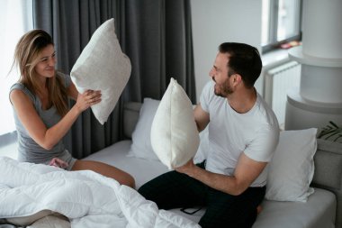 Genç çift yatakta yastık kavgası yapıyor. Mutlu çift evde eğleniyor.