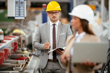 Fabrika müdürü ve mühendisi teftiş yapıyor. İş adamı ve işkadını üretim hattında.