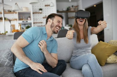 Mutlu çift oturma odasında sanal gerçeklik gözlükleriyle eğleniyor. Evde video oyunu oynayan ve eğlenen genç bir çift..