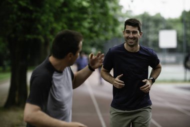 Gençler yarış pistinde antrenman yapıyor. İki genç arkadaş atletizm pistinde koşuyor.