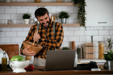 Mutfaktaki yakışıklı adamın portresi. Genç adam dizüstü bilgisayar kullanırken yemek yapıyor..
